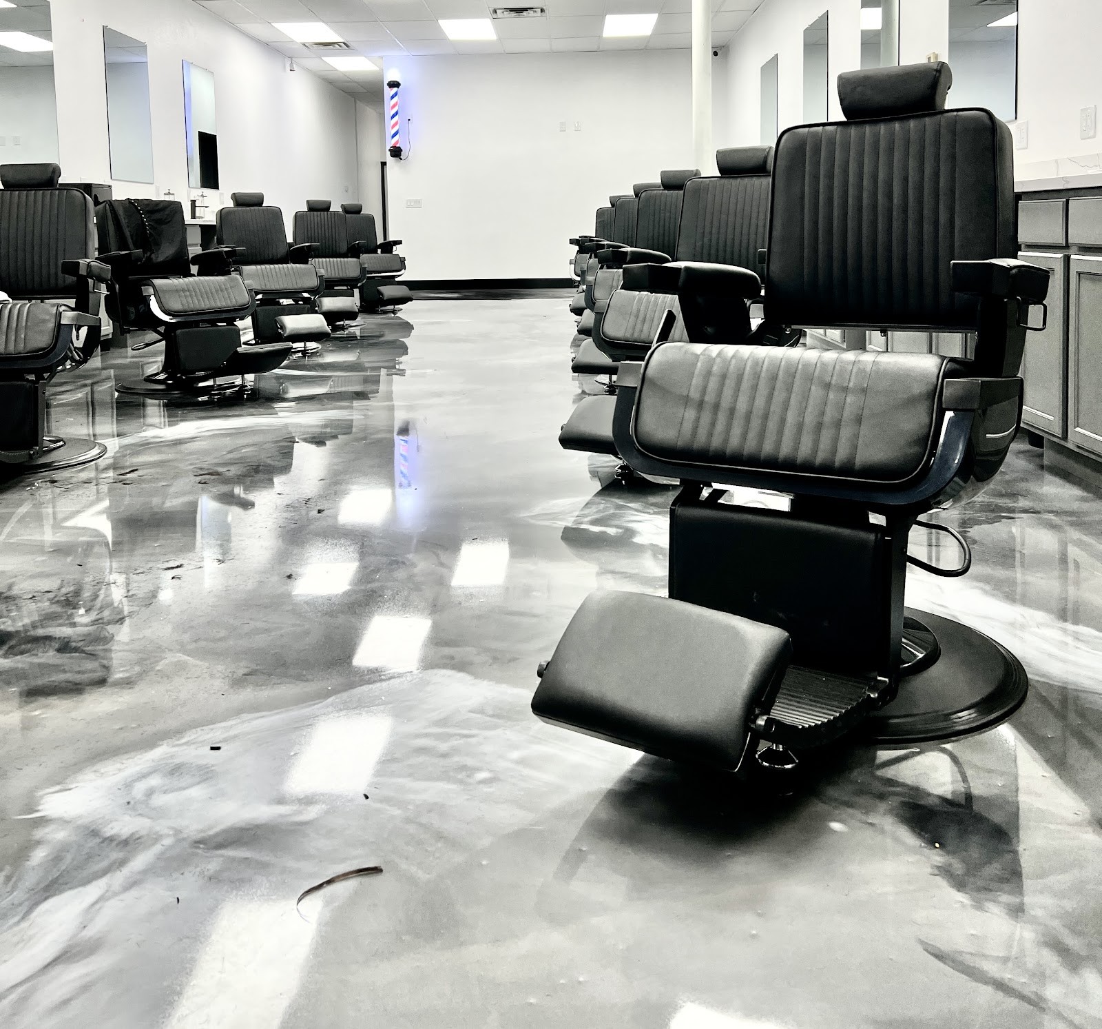 Black barber chairs and glossy silver epoxy floor with a barber pole in the background