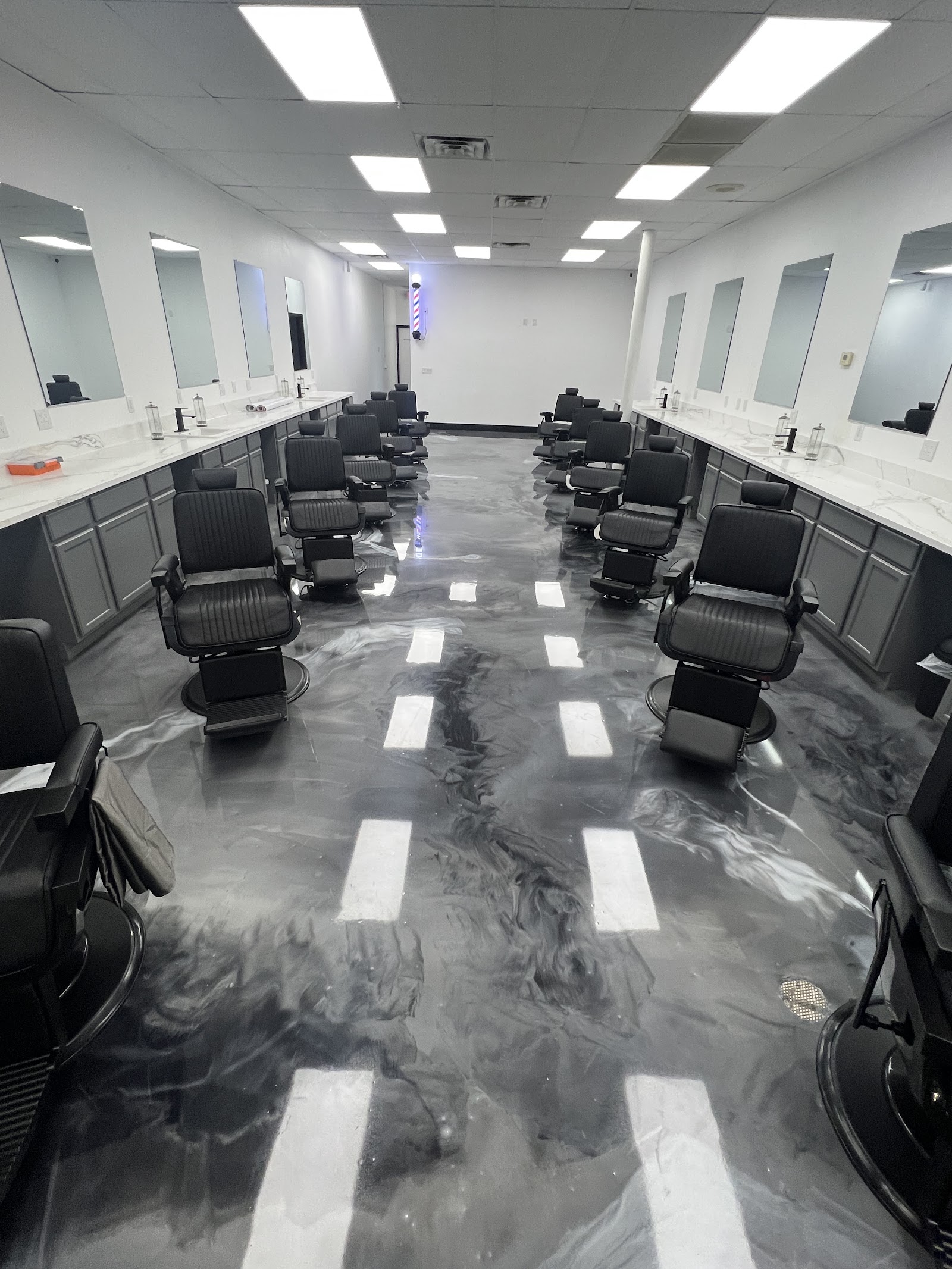 Rows of black barber chairs facing mirrors with a marble-effect epoxy floor