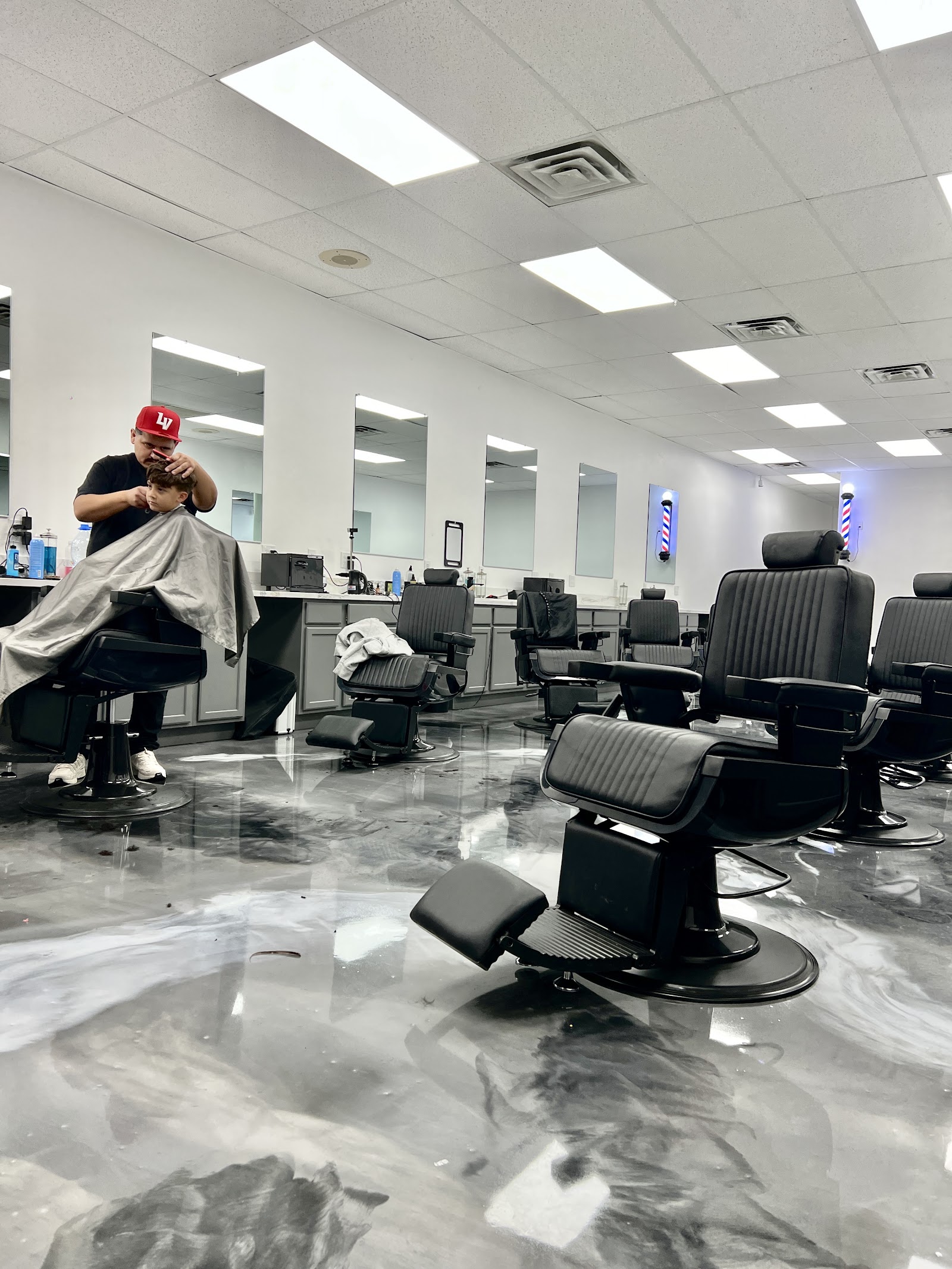 Spacious barbershop interior with a barber cutting a boy's hair and rows of black barber chairs